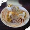 Cream-filled pastry topped with pistachios on a decorative plate, drizzled with caramel and white chocolate, showcasing delicious dessert options for travel and culinary experiences.
