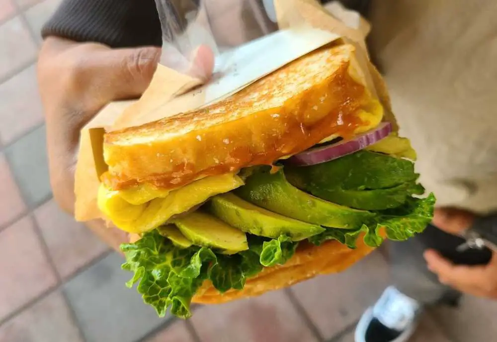 Avocado Sandwich Eggs w/ grilled corn, green leaf lettuce, avocado, and red onion on toasted brioche bread with paprika sauce and lime. Semicolon Cafe in Jersey City NJ
