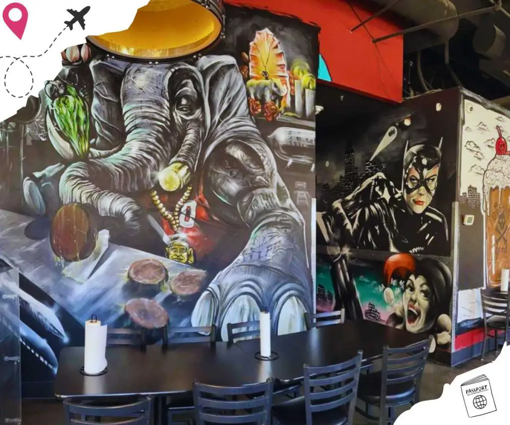 Graffiti art of an elephant, Cat Woman and Harley Quinn from DC, and a root beer float with a Jolly Roger on it adorn the walls behind the black chairs and tables.
