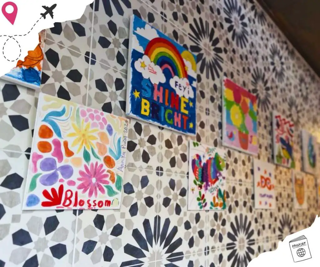 Patterned tile wall adorned across with childlike drawings on white square canvases.