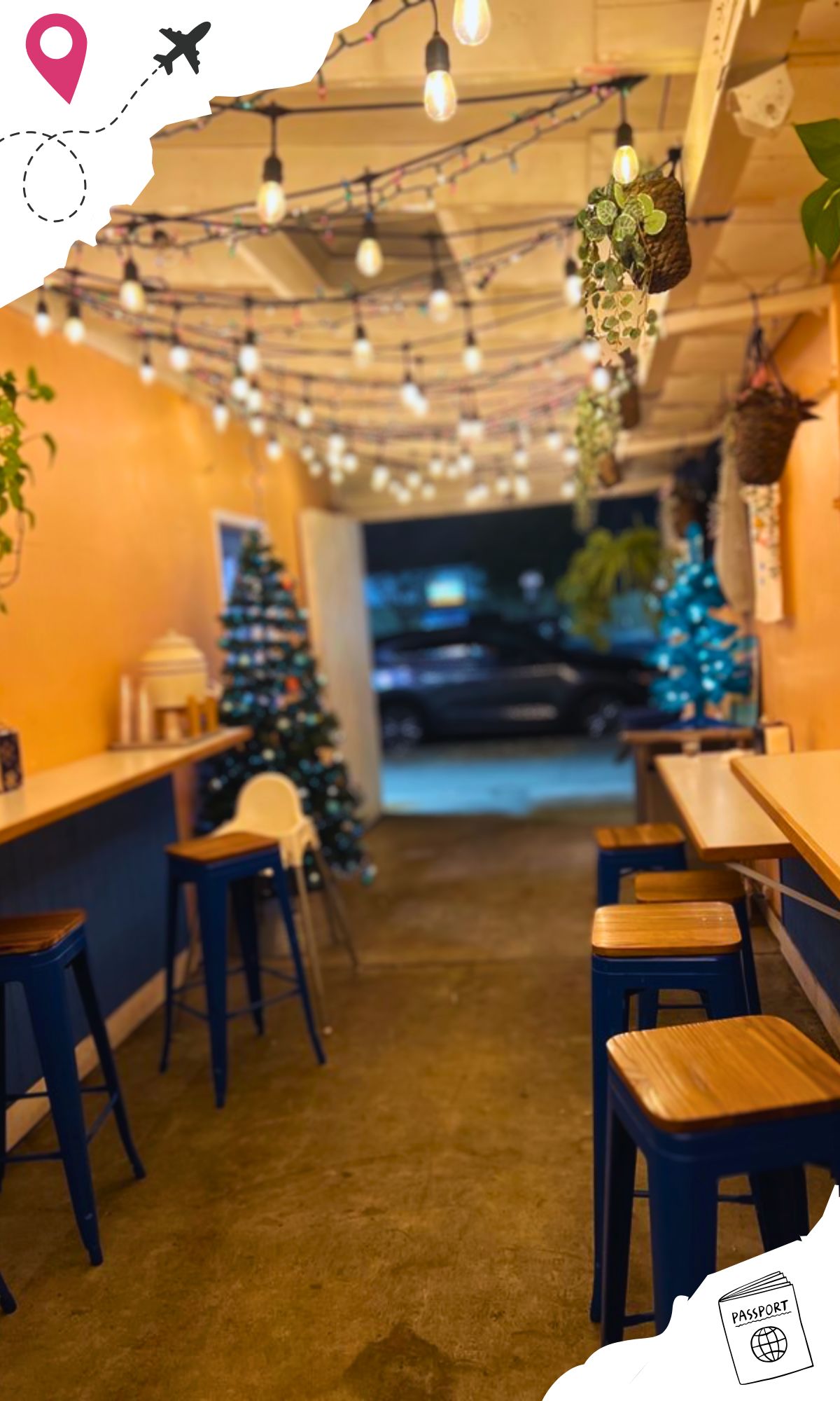 A hallway leading outdoors, topped with stringed lights and complete with a bar and stools on either side of the hallway