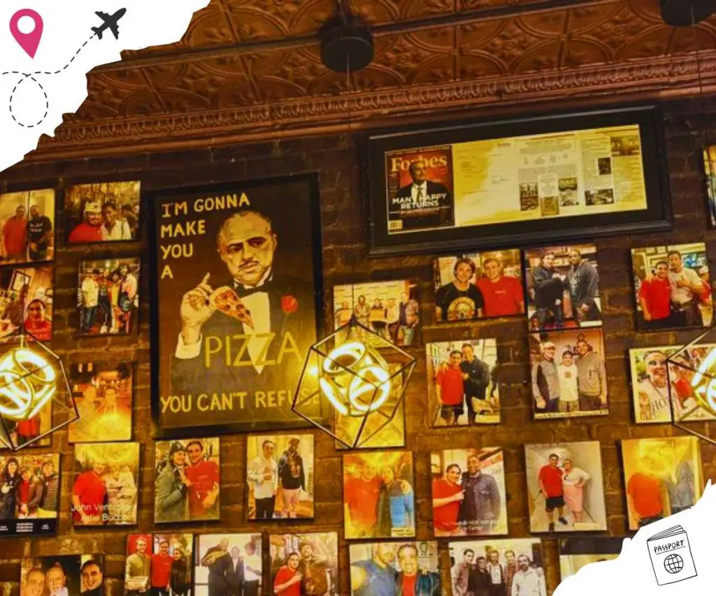 A wall of Photos with a few pages of a magazine framed, as well as a poster that reads, "I'M GONNA MAKE YOU A PIZZA YOU CAN'T REFUSE".