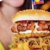 Delicious bacon cheeseburger with crispy fried onions, fresh toppings, and a small Colombian flag, served with a side of fries, highlighting American and international fast food cuisine.
