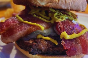 Juicy bacon cheeseburger with fresh lettuce and mustard on a toasted bun, perfect for travel food lovers seeking flavorful American cuisine.