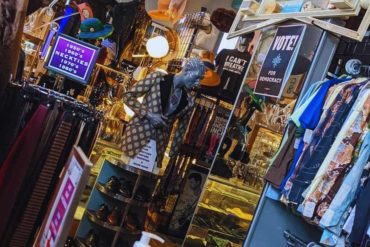 Vintage clothing store with eclectic fashion items and accessories, colorful decor, and travel-themed signs, perfect for fashionistas and travel lovers exploring unique apparel and souvenirs.