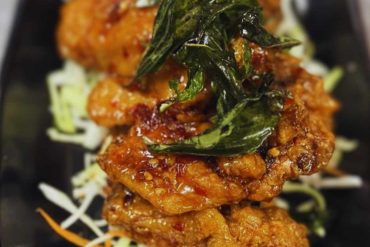 Crispy fried chicken with fresh basil garnished on leafy bed in black dish, close-up of delicious Asian-style cuisine.