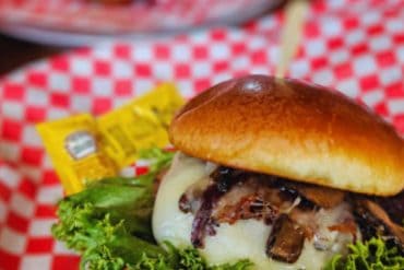 Juicy cheeseburger with melted cheese, crispy bacon, lettuce, and pickles in a toasted bun, served on red checkered paper, perfect for travel food experiences.