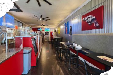 Red and black fast food restaurant interior with tables, chairs, wall art, and ceiling fans, promoting casual dining and quick service.