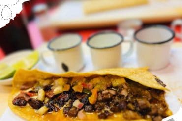 Tacos filled with seasoned meat, vegetables, and cheese on a plate with lime wedges, showcasing delicious Mexican cuisine for travel and food enthusiasts.