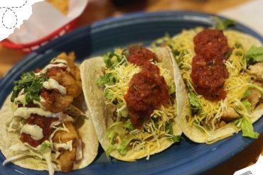 Spicy chicken tacos with shredded cheese and fresh greens on a blue plate, served with a side of chips, perfect for a flavorful Mexican meal experience.