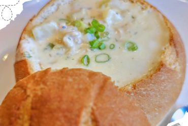 Creamy crab and scallop chowder served in a bread bowl with green onions on top, ideal for travel food experiences.