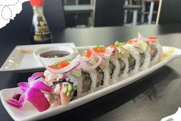 Fresh sushi rolls with colorful garnishes served on a white platter at an airport lounge, accompanied by soy sauce and wasabi. Perfect for travelers seeking delicious cuisine before a flight.