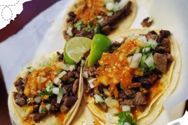 Beef tacos with chopped onions, cilantro, spicy sauce, and lime wedges on a soft corn tortilla, traditional Mexican street food, close-up shot for Mexican cuisine lovers.