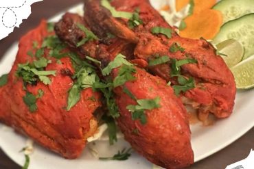 Spicy grilled chicken (tandoori style) garnished with fresh cilantro and served with lemon, cucumber, and carrot slices on a white plate, ideal for Indian cuisine lovers, travel, and food destinations.
