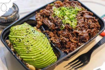 Sliced avocado with sesame seeds and chopped green onions served with beef bulgogi in a black lunch box, Asian cuisine, healthy food, meal prep, Korean dishes, food photography, GotoDestinations.