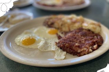 Scrambled eggs with sunny-side-up eggs, crispy hash browns, and country sausage patty on a beige plate, showcasing a hearty breakfast.