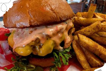 Cheeseburger with fries served in a casual restaurant setting, featuring melted cheese, fresh vegetables, and seasoned potato fries for a classic American dining experience.
