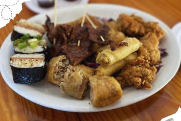 Sushi rolls, fried spring rolls, and crispy chicken drumsticks served on a white plate, highlighting Asian cuisine and food travel experiences.