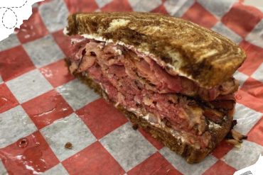 Succulent, crispy Reuben sandwich with corned beef, sauerkraut, and melted cheese on toasted rye bread, served on red checkered paper at a local diner, perfect for travel food adventures.