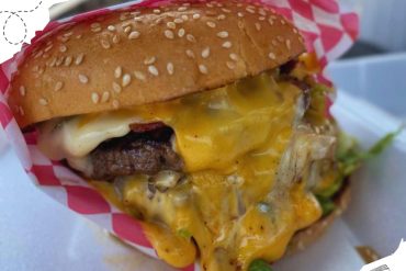 Succulent cheeseburger with melted cheese, beef patty, fresh lettuce, and toasted sesame bun, served with a paper liner for an authentic fast food experience.