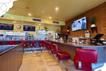 Cozy diner interior with red booth seats, brick wall decor, and a television showing a black-and-white movie, perfect for a casual dining experience.