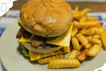 Crispy bacon cheeseburger with fries on plate at a travel-themed setting.