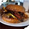 Savory burger with bacon, cheese, and toasted bun on a white plate at a restaurant, popular travel food destination, delicious gourmet burger for travel and adventure seekers, vibrant food photography for travel blogs.