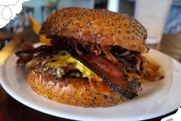 Savory burger with bacon, cheese, and toasted bun on a white plate at a restaurant, popular travel food destination, delicious gourmet burger for travel and adventure seekers, vibrant food photography for travel blogs.