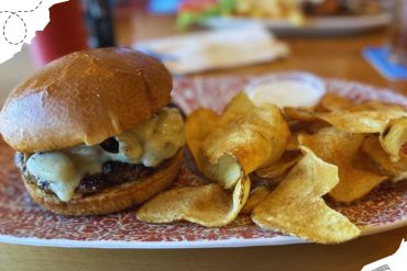 Beef cheeseburger with melted cheese, served with crispy potato chips on a decorative tray at a casual restaurant. Perfect for food lovers and burger enthusiasts exploring new dining destinations.