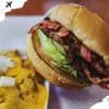 Smoked brisket sandwich with crispy bacon, fresh lettuce, and toasted bread served with a side of cheesy scrambled eggs topped with chopped onions, showcasing delicious American comfort food.