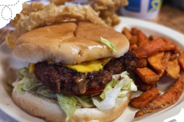 Buttermilk biscuit breakfast sandwich with beef sausage, cheddar, egg, lettuce, tomato, and waffle fries on white plate at rustic restaurant, comfort food, American breakfast, hearty meal, casual dining, go to destinations, USA.