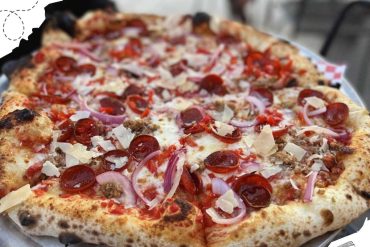 Delicious pepperoni and sausage pizza with onions and cheese, served on a metal tray, showcasing popular Italian-style cuisine at a travel destination.