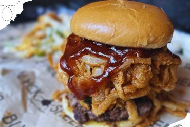 Succulent fried chicken sandwich with crispy onions and barbecue sauce, served on a soft bun at a travel-inspired eatery. Ideal for food lovers exploring tasty destinations and culinary adventures.