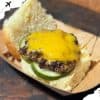 Crispy cheeseburger with melted cheddar, fresh cucumber slices, and toasted bun on a wooden table.