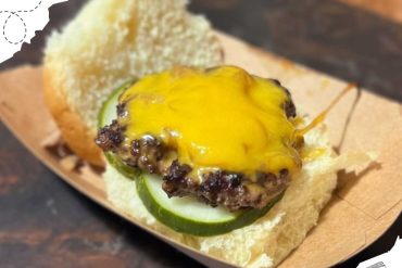 Crispy cheeseburger with melted cheddar, fresh cucumber slices, and toasted bun on a wooden table.