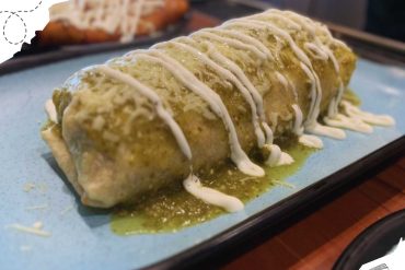 Oaxaca cheese enchilada with green sauce and white cheese drizzle on a blue plate for Mexican cuisine.