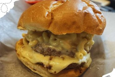 Succulent cheeseburger with melted cheese, beef patty, creamy macaroni topping, and toasted bun on parchment paper, perfect for travel-focused foodies and culinary travel enthusiasts.