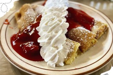 Creamy cannoli dessert with whipped cream topping, powdered sugar, and cherry topping on a baked pastry shell, perfect for Italian cuisine lovers and dessert enthusiasts.