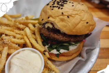 Juicy burger with fresh toppings, crispy French fries, and creamy dipping sauce served on a metal platter for a satisfying meal. Perfect for food lovers exploring new dining destinations.