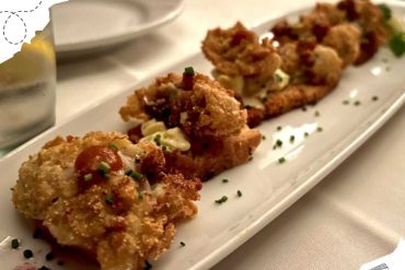 Crispy fried chicken bites served with creamy sauce on a long white platter, garnished with chopped herbs, perfect for a gourmet dining experience.