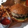 Crispy sesame seed bun cheeseburger with melted cheese and fresh greens, served with seasoned French fries and ketchup, ideal for travel food lovers and burger enthusiasts.