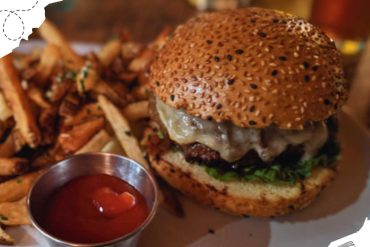 Crispy sesame seed bun cheeseburger with melted cheese and fresh greens, served with seasoned French fries and ketchup, ideal for travel food lovers and burger enthusiasts.