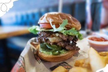 Juicy cheeseburger with fresh lettuce, tomato, and pickles on a toasted bun served with crispy fries and dipping sauce. Perfect for food lovers seeking delicious American cuisine.