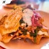 Crispy taco salad topped with sour cream, shredded cheese, fresh cilantro, and pickled red onions, served on a white plate for an authentic Mexican cuisine experience.