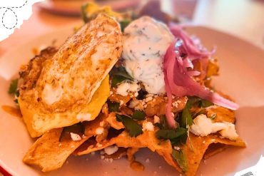 Crispy taco salad topped with sour cream, shredded cheese, fresh cilantro, and pickled red onions, served on a white plate for an authentic Mexican cuisine experience.