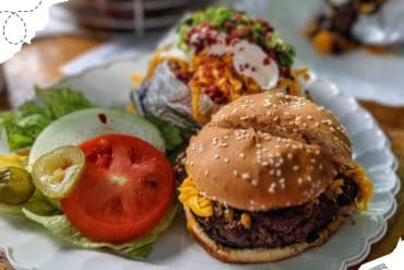 Beef burger with lettuce, tomato, pickles, and side salad on white plate, fast food meal, American cuisine, casual dining, delicious comfort food, popular restaurant dish, Go To Destinations travel concept, road trip food, culinary travel photos.