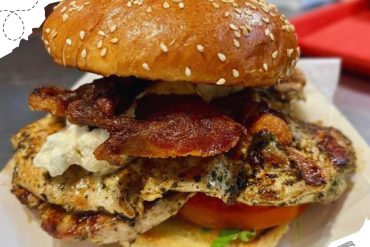 Succulent grilled chicken and crispy bacon burger with fresh vegetables on a sesame seed bun, perfect for travel food or dining out in international destinations.