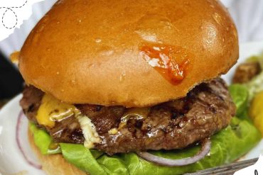 Juicy beef burger with melted cheese, fresh lettuce, and red onions on a toasted bun, perfect for exploring local foods on your travel adventures.