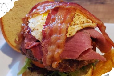 Succulent burger topped with crispy bacon, fried egg, and fresh greens, served on a toasted bun, perfect for travel food enthusiasts exploring diverse cuisines around the world.