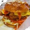 Crispy fried chicken sandwich with melted cheese, fresh lettuce, tomato, and spicy sauce on a shiny bun, served with shredded cheese and shredded lettuce underneath, delicious comfort food option.